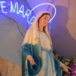 Elegant statue of Virgin Mary under a neon 'Ave Maria' sign with floral decor.