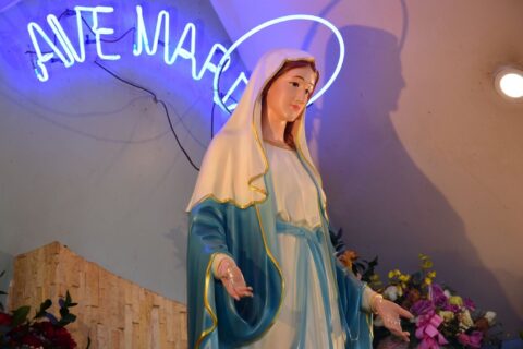 Elegant statue of Virgin Mary under a neon 'Ave Maria' sign with floral decor.