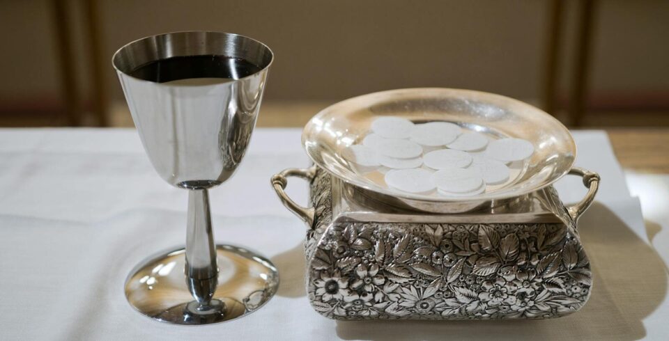 Elegant display of a silver chalice with wine and wafers in a sacred setting, symbolizing the Eucharist.