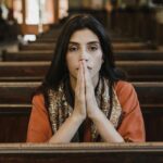 A woman in a church pew with folded hands, symbolizing faith, prayer, and contemplation.