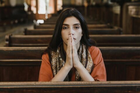 A woman in a church pew with folded hands, symbolizing faith, prayer, and contemplation.