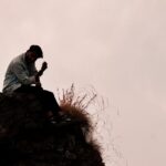 a man sitting on top of a rock next to a grass covered hillside