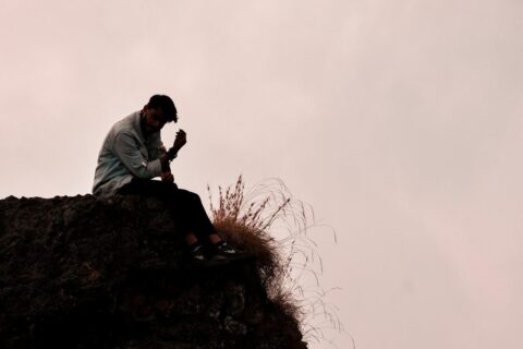 a man sitting on top of a rock next to a grass covered hillside