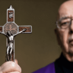 Otac Gabriele Amorth drži raspelo tijekom molitve, dok je križ u prvom planu kao simbol Kristove pobjede nad zlom.