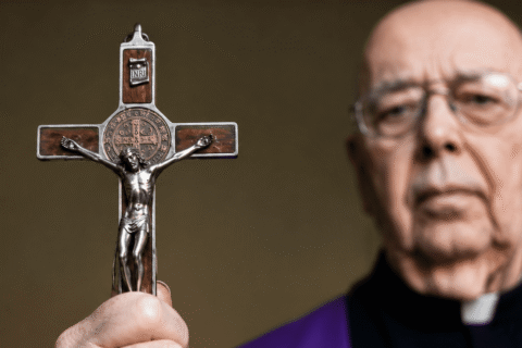 Otac Gabriele Amorth drži raspelo tijekom molitve, dok je križ u prvom planu kao simbol Kristove pobjede nad zlom.