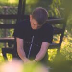 selective focus photography of sitting man wearing black cross graphic shirt