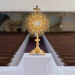 A golden monstrance with candles on an altar.