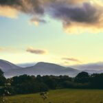 green grass field near mountain under cloudy sky during daytime