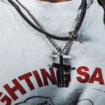 Close-up of a man wearing a cross necklace and graphic T-shirt, showcasing trendy jewelry.