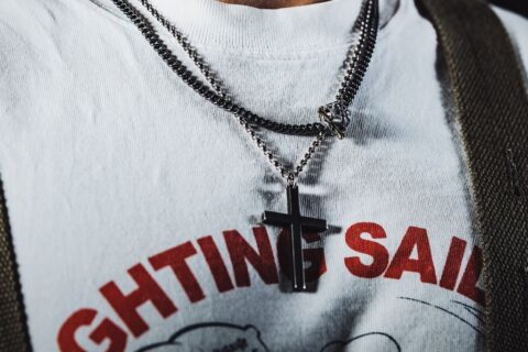 Close-up of a man wearing a cross necklace and graphic T-shirt, showcasing trendy jewelry.