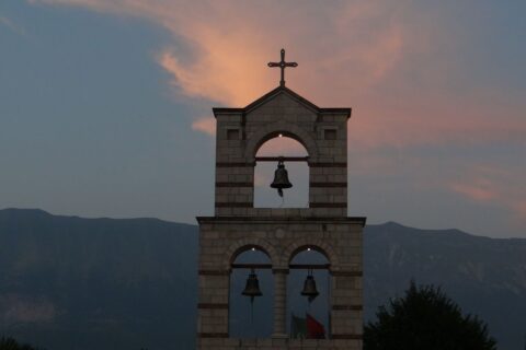 Crkvena zvona: Njihova prava svrha u liturgiji i životu Crkve A tranquil view of a bell tower with a cross against sunset skies and distant mountains.