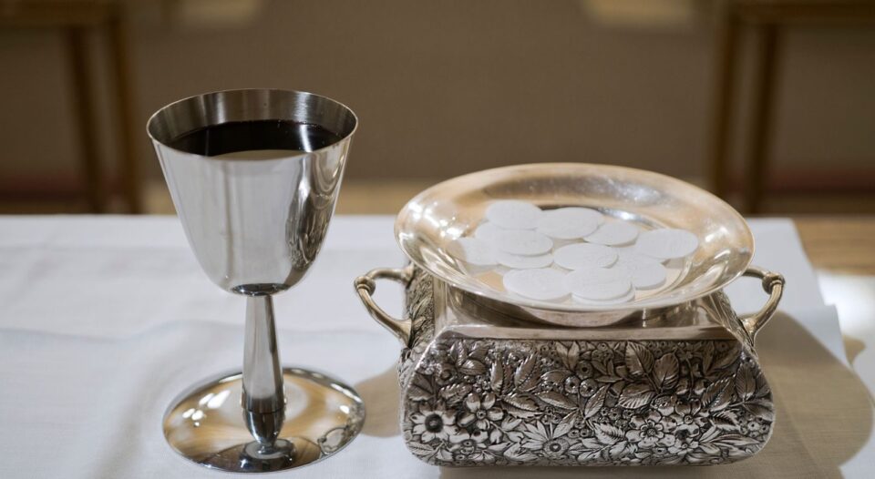 Elegant display of a silver chalice with wine and wafers in a sacred setting, symbolizing the Eucharist.