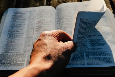 a person holding an open book on top of a wooden table