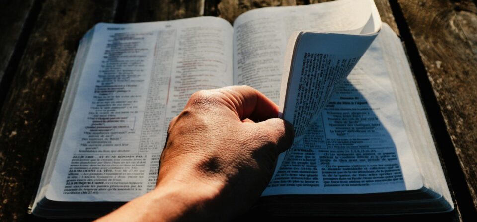 a person holding an open book on top of a wooden table