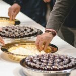 People reaching for desserts on a table.
