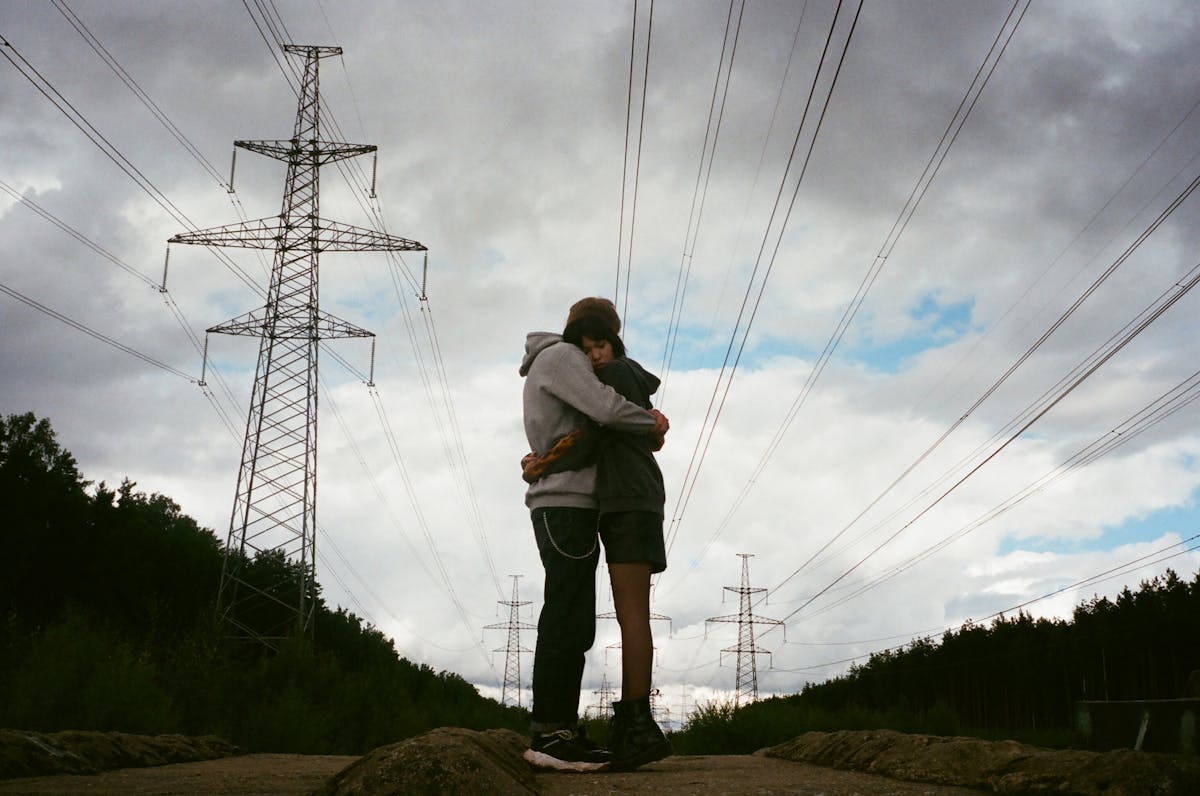Couple hugging beneath power lines under a cloudy sky, showcasing a moment of affection and connection.