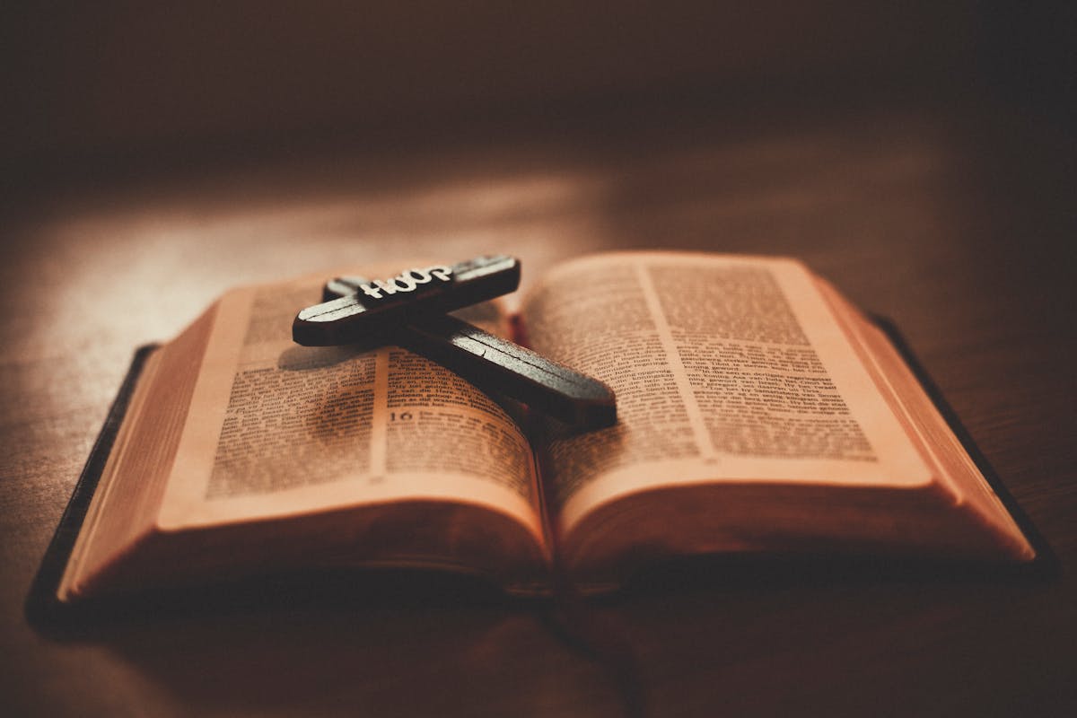 Close-up of an open Bible with a wooden cross inscribed with 'Hope' on a table.