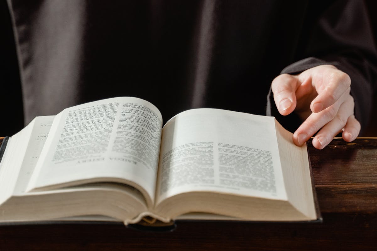 Close-up of a person turning pages of an open Bible on a wooden desk.