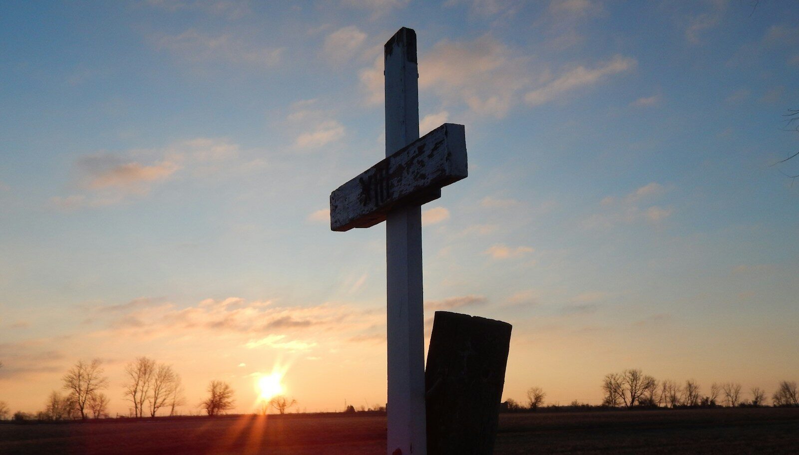 a cross in a field with the sun setting in the background