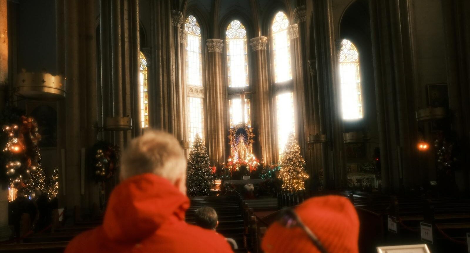 Visitors in a cathedral admire the altar adorned with Christmas decorations and sunlight.