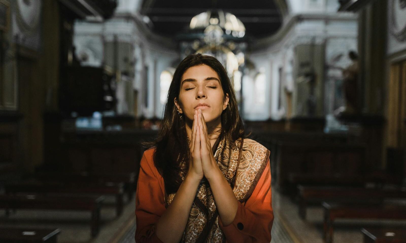 A woman with closed eyes prays in a peaceful cathedral setting, conveying a sense of calm and spirituality.
