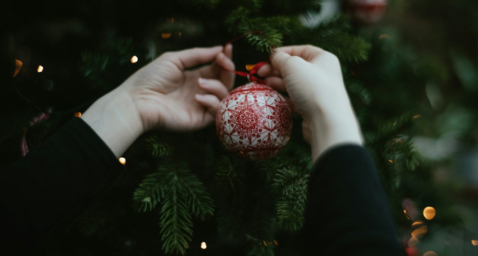 two hands holding a christmas ornament in front of a christmas tree