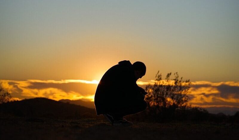 a silhouette of a person sitting on a hill at sunset