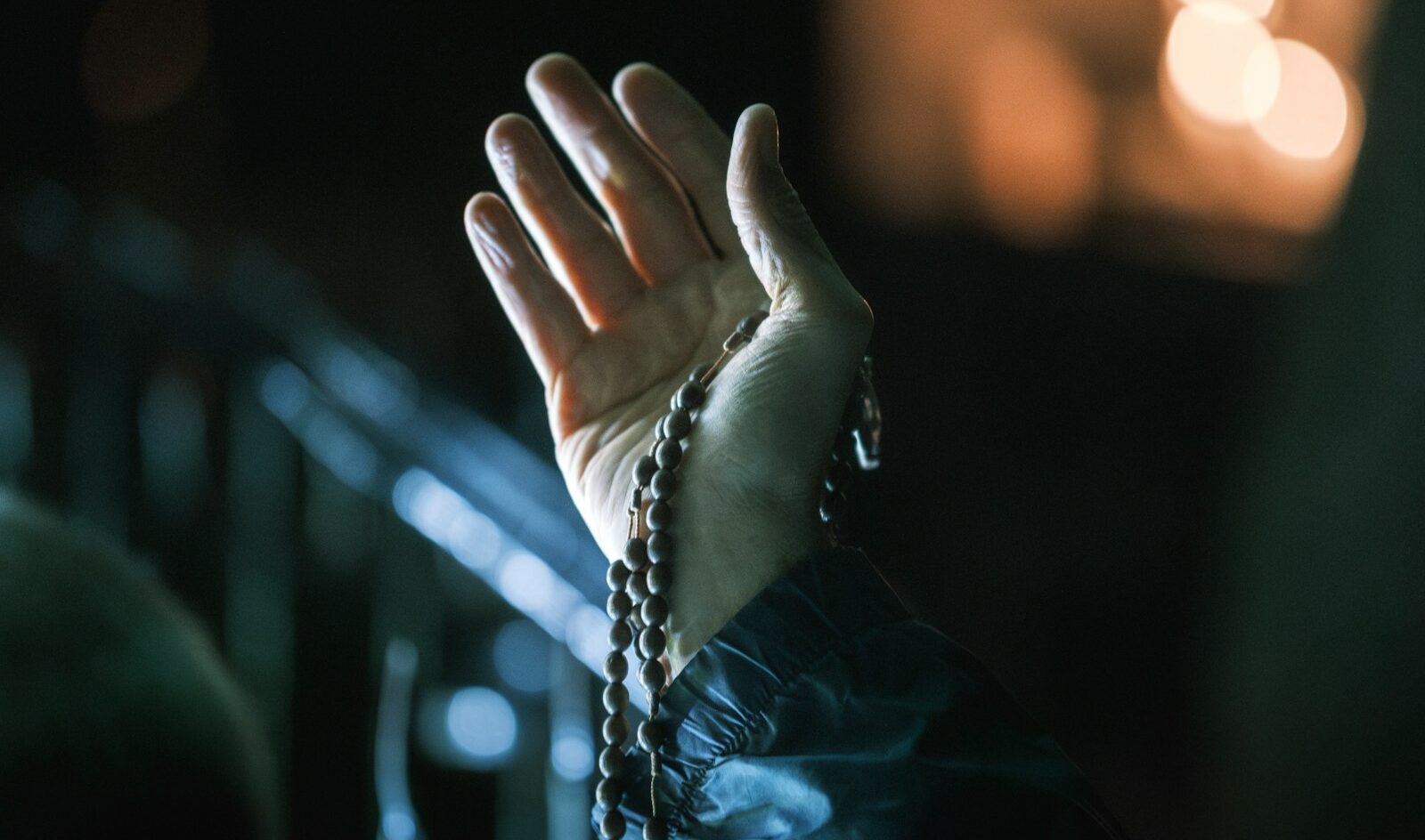 Hand holding rosary beads in dim light