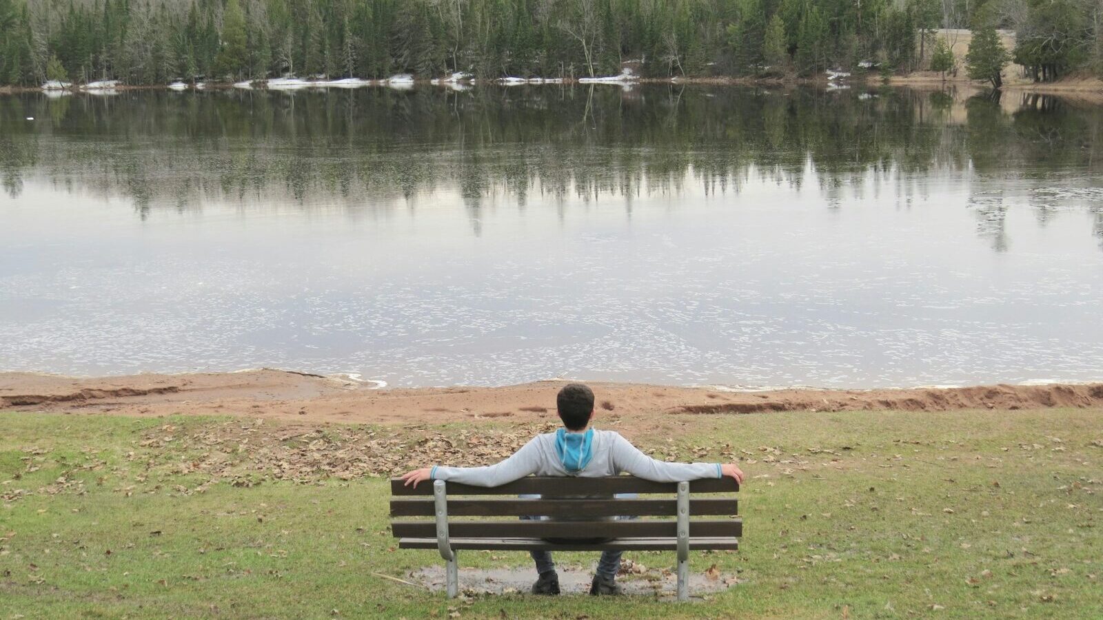 woman sitting on bench near lake during daytime