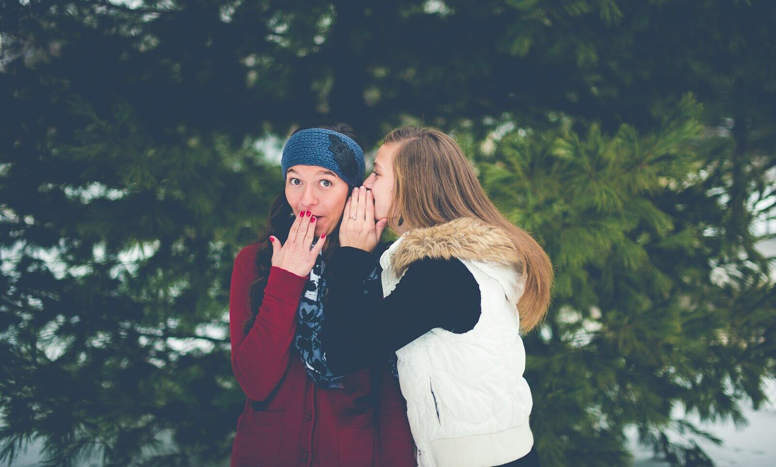 woman whispering on woman's ear while hands on lips