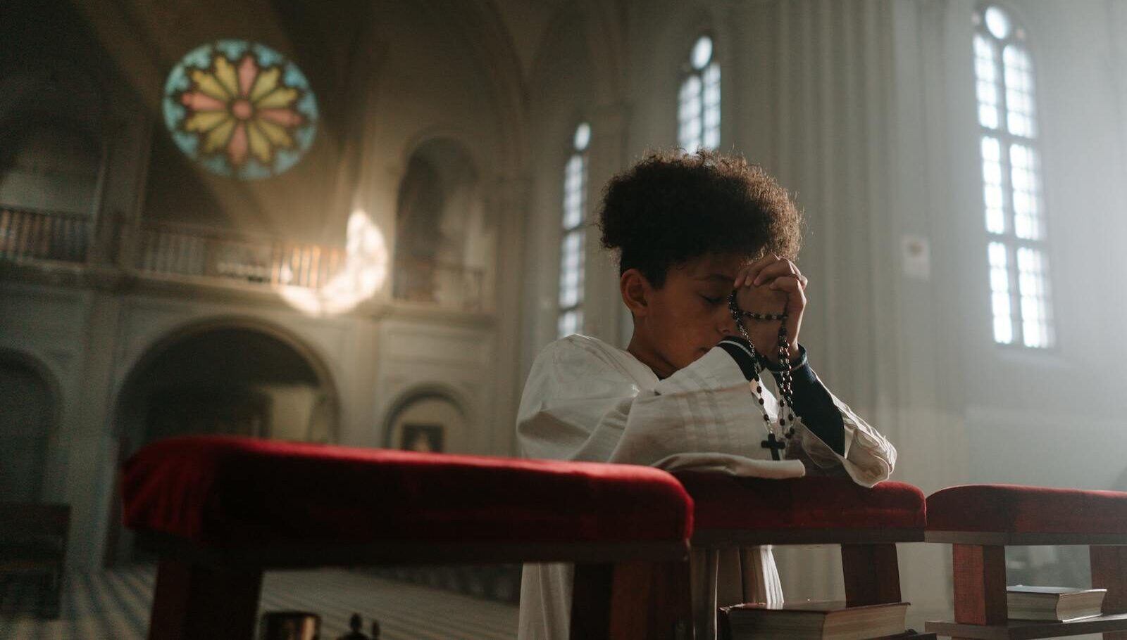 Child praying with rosary in a serene cathedral setting, sunlight through stained glass.