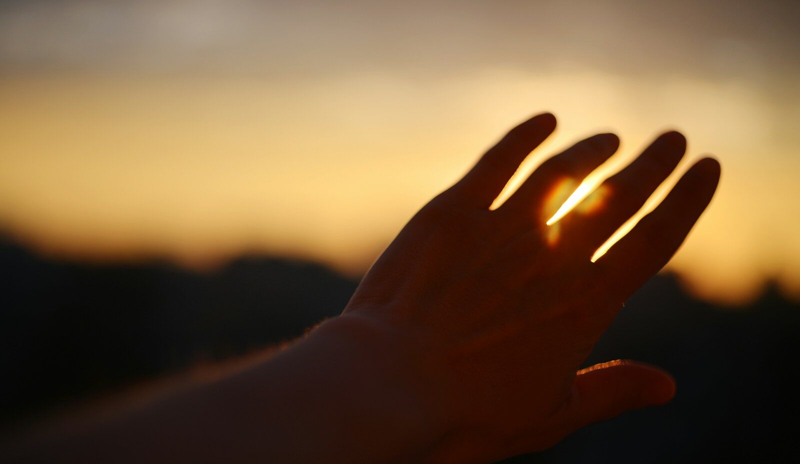 Hand blocks the setting sun, creating a silhouette.