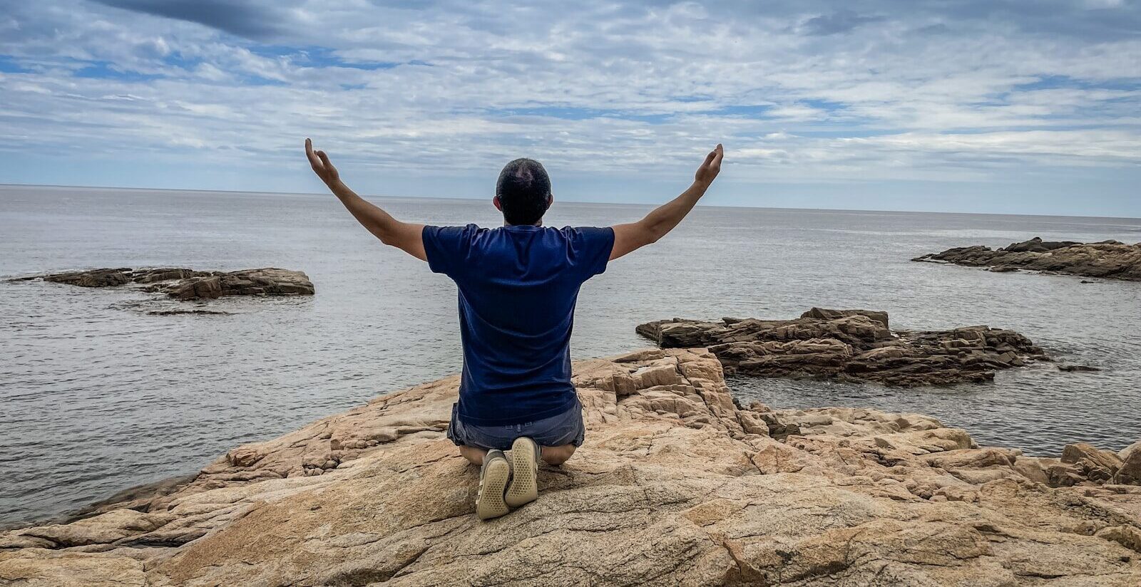 a man sitting on top of a rock near the ocean
