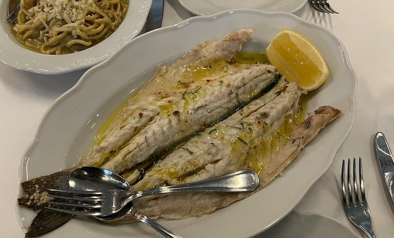 a white plate topped with fish next to a bowl of noodles