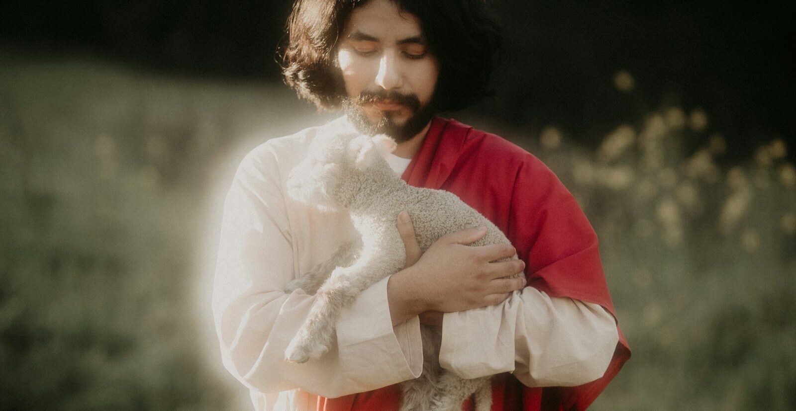 Man in robes holding a lamb in a field