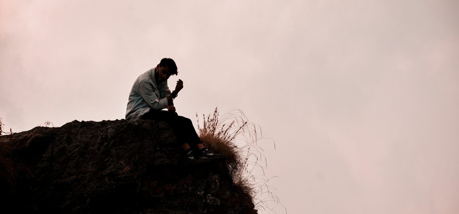 a man sitting on top of a rock next to a grass covered hillside