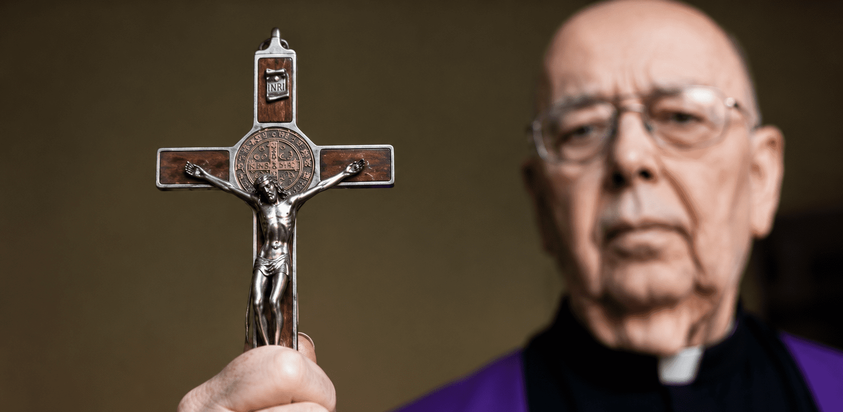 Otac Gabriele Amorth drži raspelo tijekom molitve, dok je križ u prvom planu kao simbol Kristove pobjede nad zlom.
