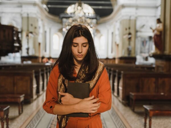 A woman in a church stands with a book, expressing contemplation and introspection.