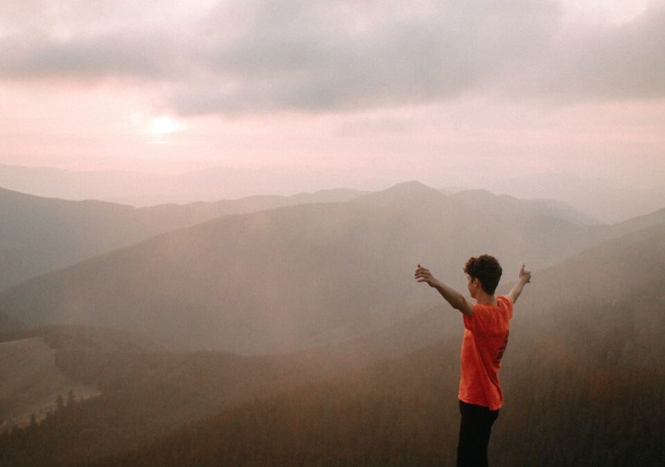 A hiker stands triumphantly on a mountain peak at sunset, enveloped in mist and nature.
