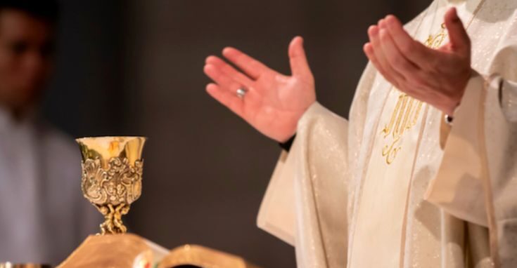 Svećenik tijekom svete mise moli raširenih ruku pokraj oltara na kojem se nalaze kalež, Biblija i liturgijske knjige.