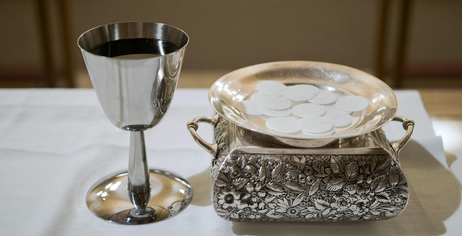 Elegant display of a silver chalice with wine and wafers in a sacred setting, symbolizing the Eucharist.