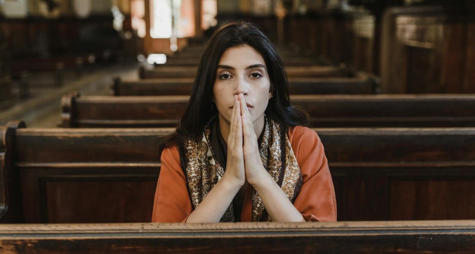 A woman in a church pew with folded hands, symbolizing faith, prayer, and contemplation.