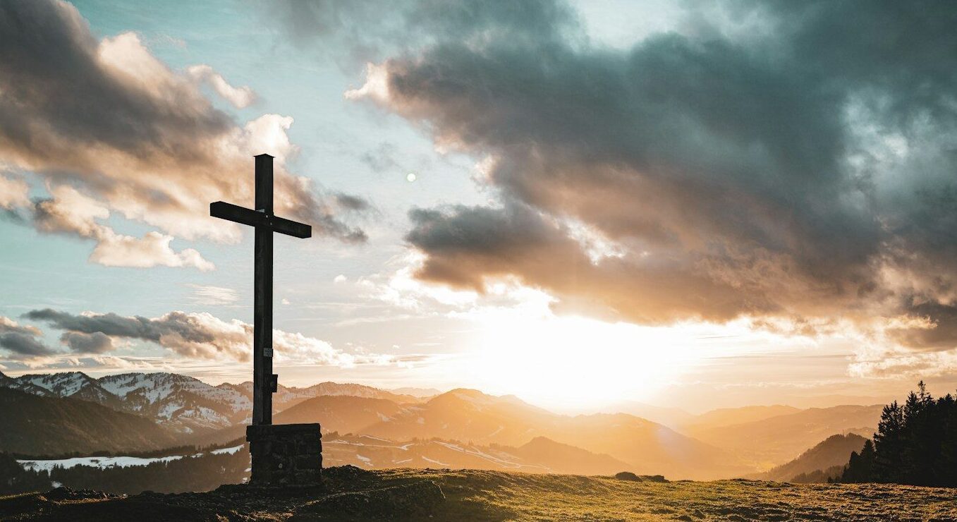 a cross sitting on top of a lush green hillside