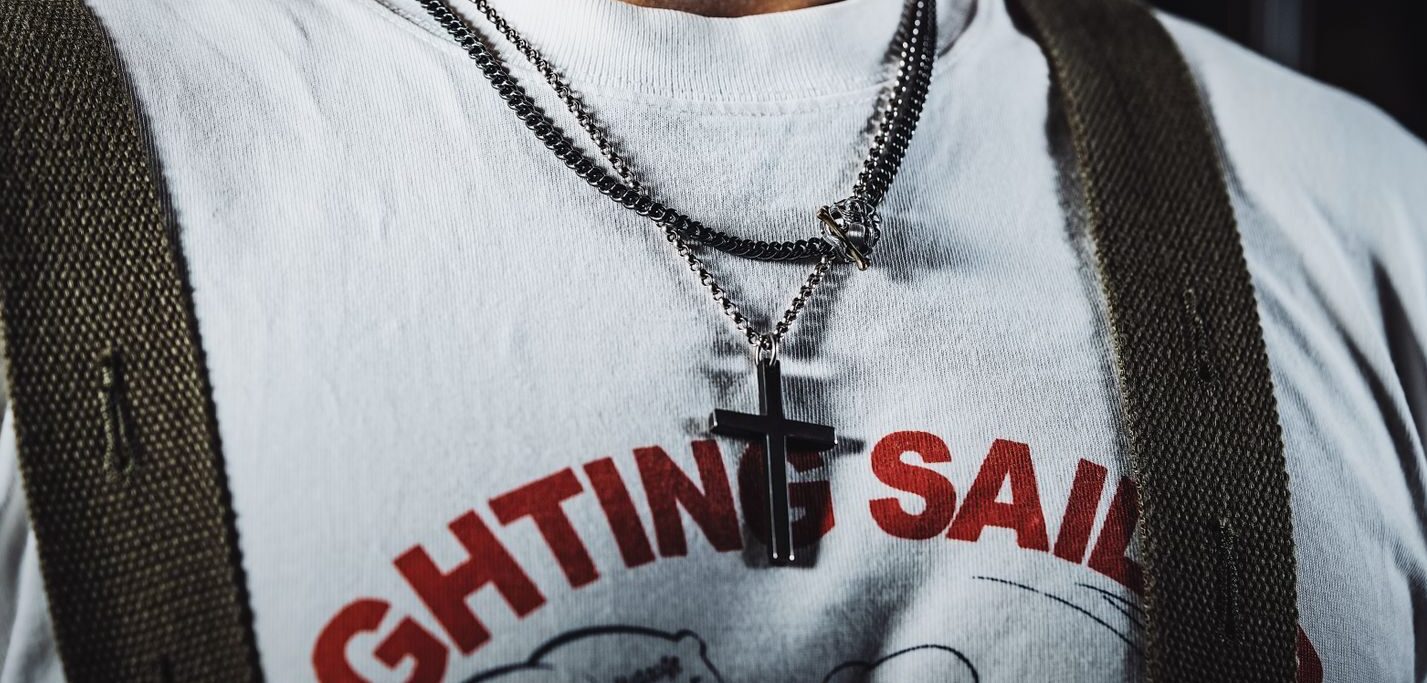 Close-up of a man wearing a cross necklace and graphic T-shirt, showcasing trendy jewelry.