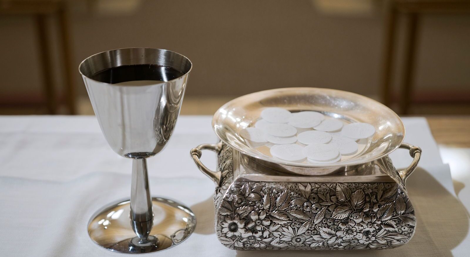 Elegant display of a silver chalice with wine and wafers in a sacred setting, symbolizing the Eucharist.