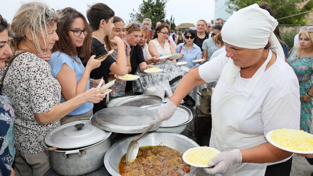 People enjoying a communal meal outdoors, served by a person in traditional attire.
