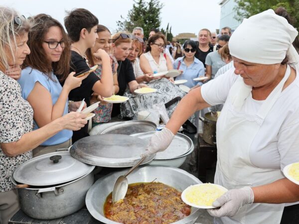 People enjoying a communal meal outdoors, served by a person in traditional attire.