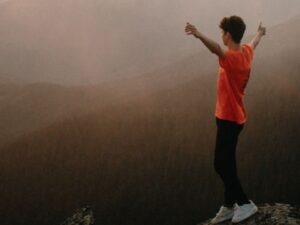 A hiker stands triumphantly on a mountain peak at sunset, enveloped in mist and nature.