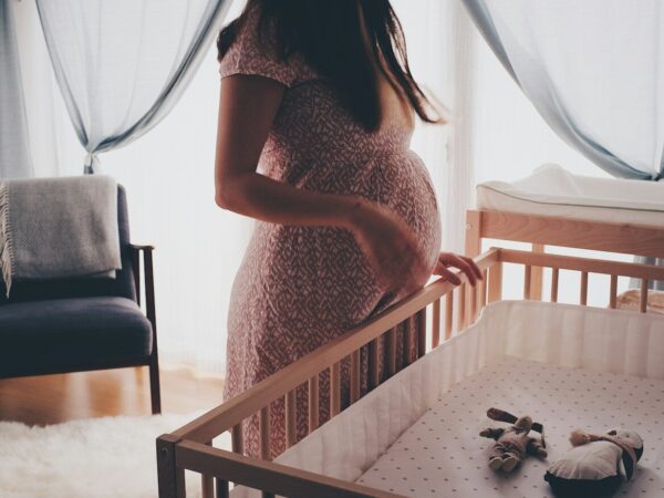 A pregnant woman standing by a wooden crib in a sunlit nursery