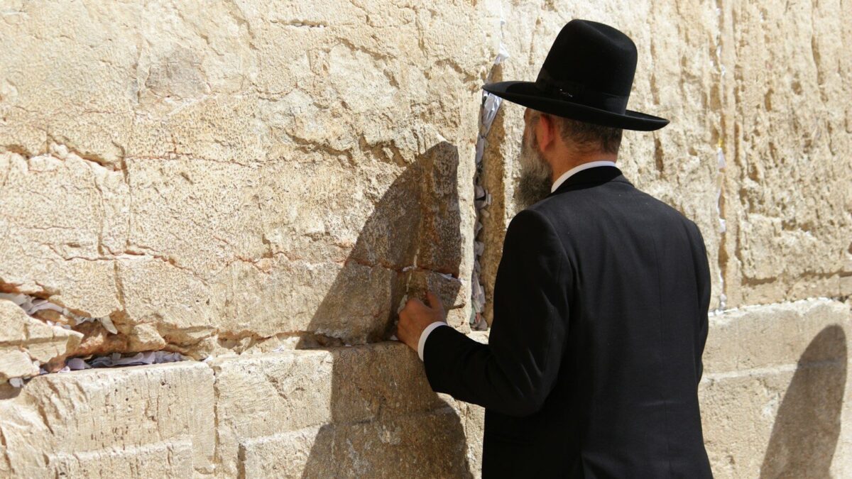 man in black long sleeve shirt and brown cowboy hat standing beside brown concrete wall during